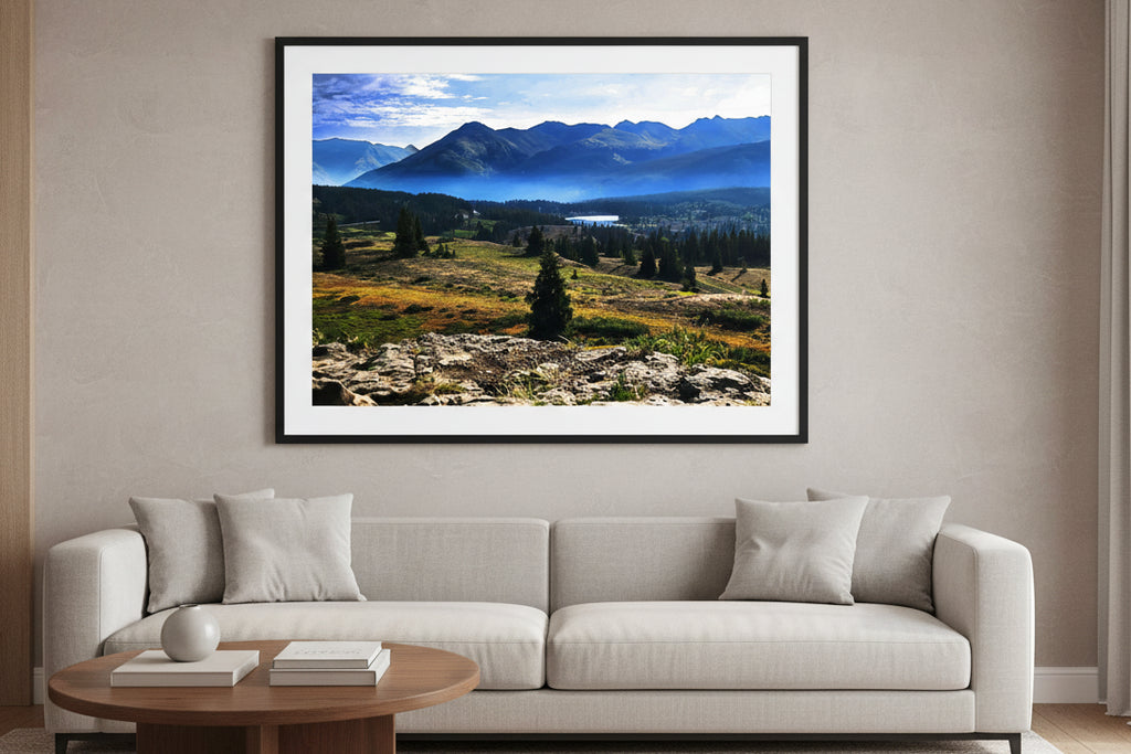 Fine art photography print of a misty morning over the Colorado Rocky Mountains with a sunlit alpine meadow and a distant valley lake.