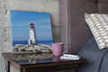 square canvas print of a lighthouse on a rocky shore under a blue sky,