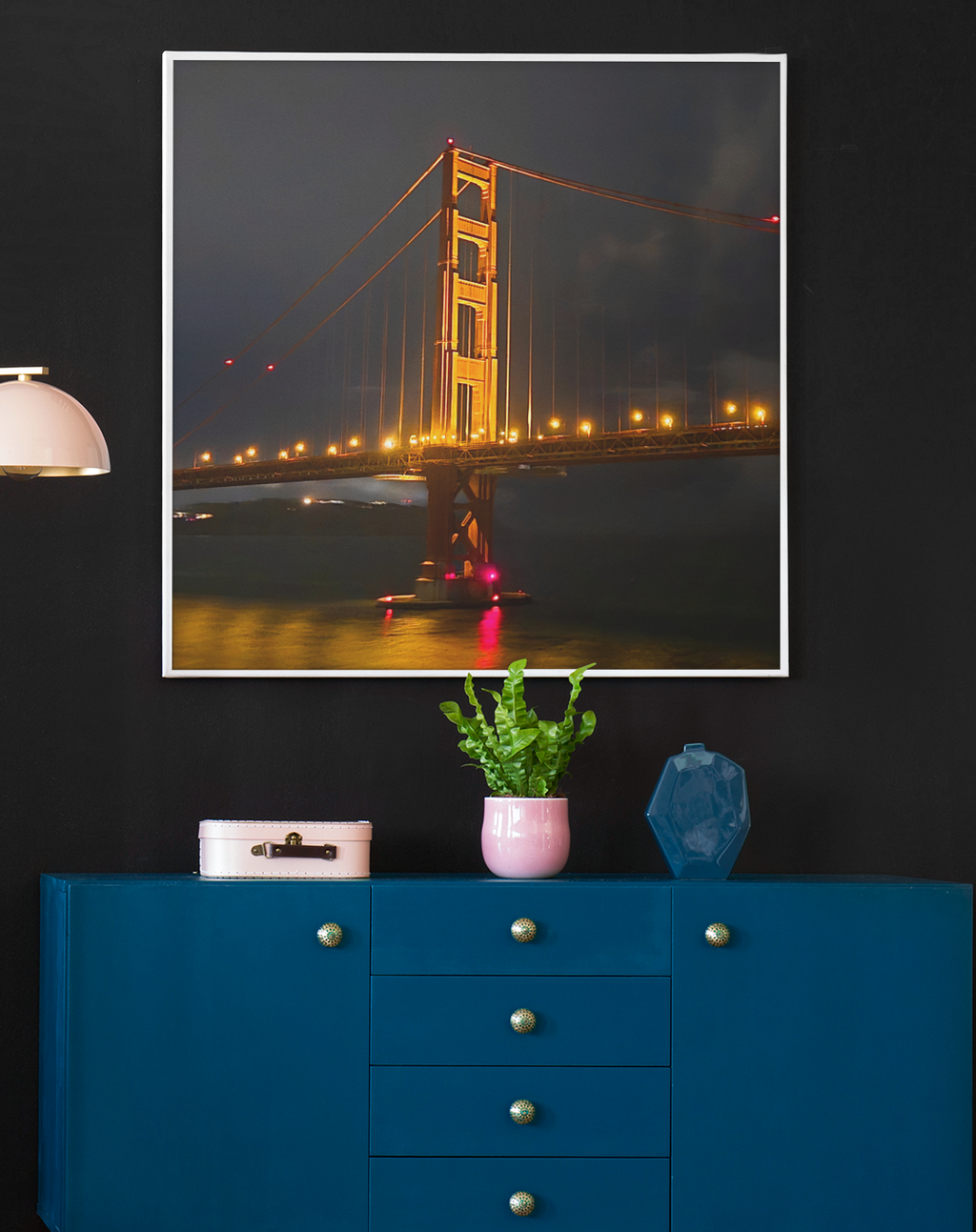 Night photography of the Golden Gate Bridge illuminated in gold against a dark clouded sky, casting glowing reflections on the water below.