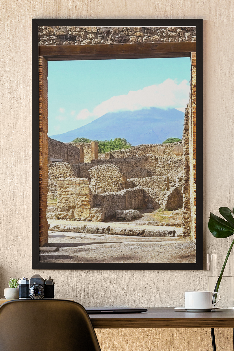 Unframed fine art photograph of ancient stone ruins in Pompeii looking out toward Mount Vesuvius under a soft blue sky.